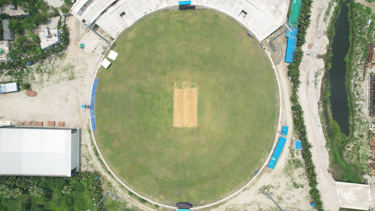Top-down view of a cricket stadium in Dhaka, showcasing the pitch and surrounding areas.