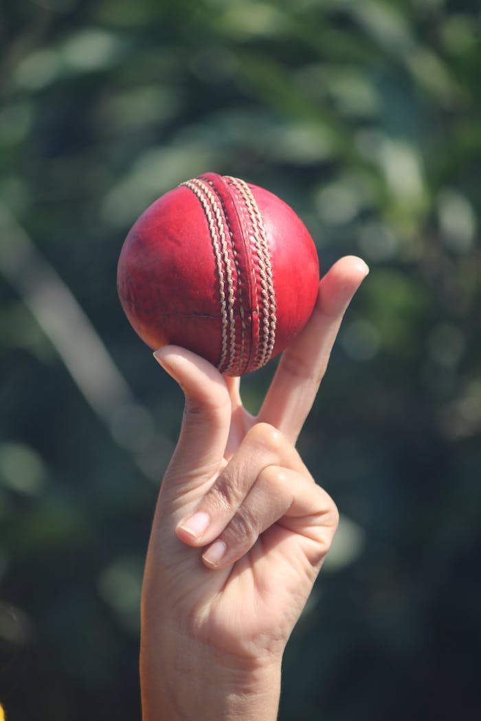 Behind the Scenes: The Unseen Force Driving Jubail Cricket A red cricket ball balanced on fingers outdoors in Jabalpur, India.